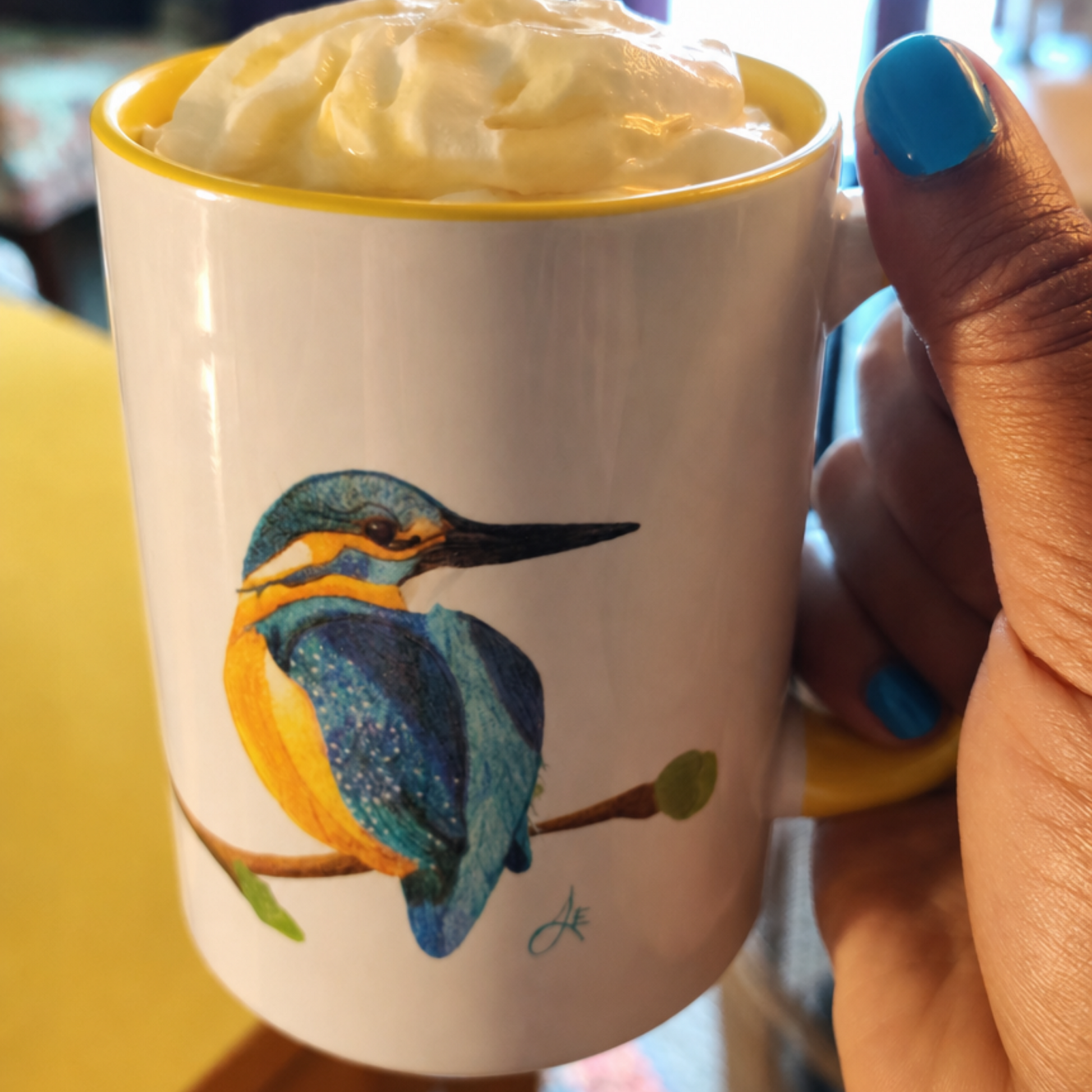 Mug with a kingfisher design held by a hand with blue nail polish.