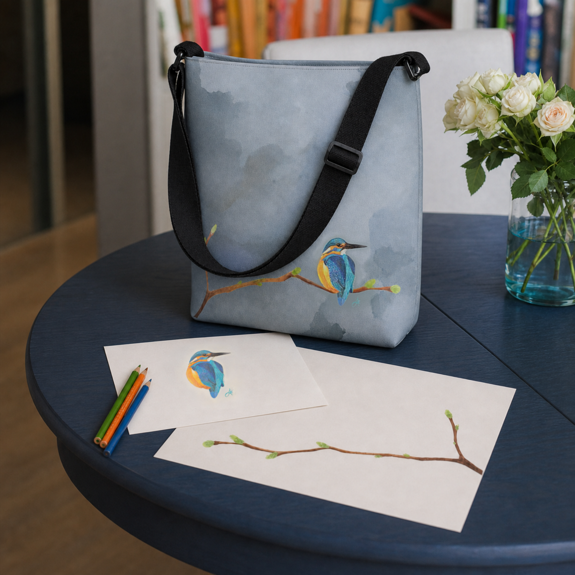 Handbag with bird design on a table with art supplies and flowers.